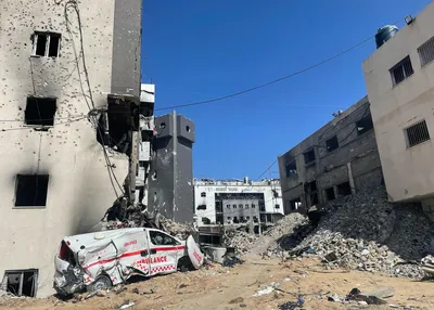 A destroyed ambulance sits in front of piles of rubble among the severely damaged buildings at a hospital in Gaza.