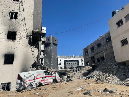 A destroyed ambulance sits in front of piles of rubble among the severely damaged buildings at a hospital in Gaza.