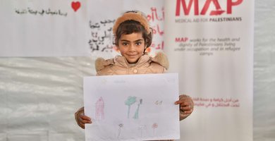 A young girl at the Solidarity Polyclinic holding up a drawing she made