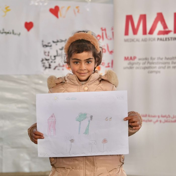 A young girl at the Solidarity Polyclinic holding up a drawing she made