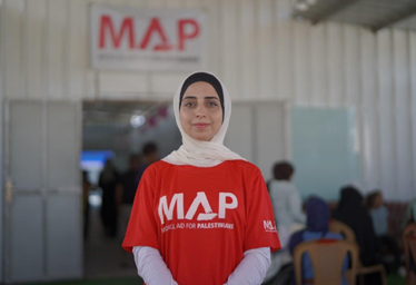 A woman wearing a white hijab and a red MAP t shirt smiles at the camera