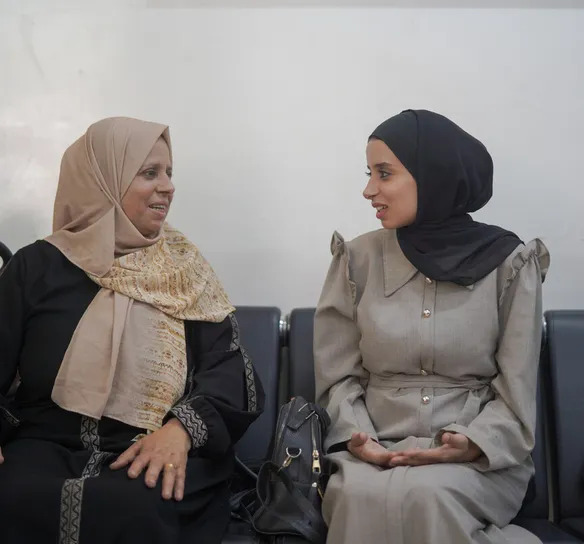 Two women sit chatting in a waiting room.