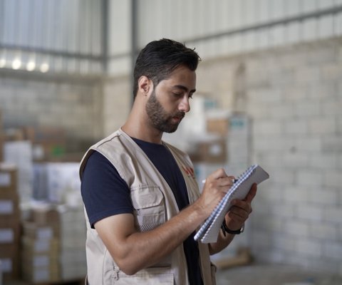 A girl wearing a red winter coat stands facing the camera supported by a metal walking frame.