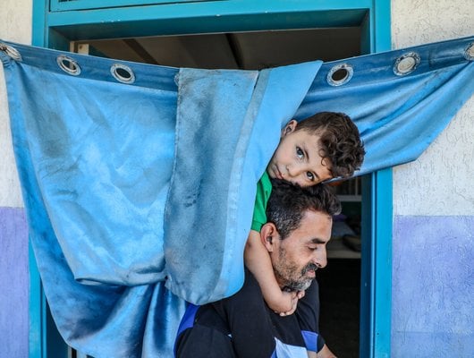 A young Palestinian boy sits on his father's shoulders and looks at the camera.
