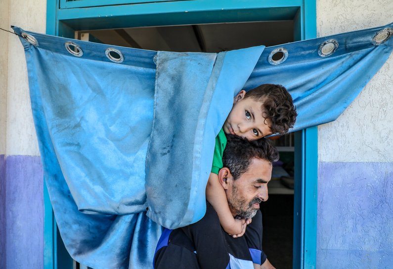 A young Palestinian boy sits on his father's shoulders and looks at the camera.