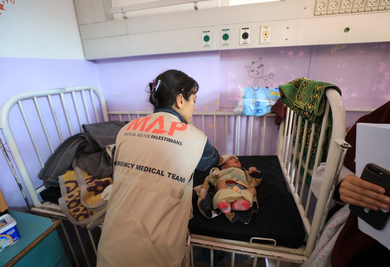A medical professional wearing a MAP vest leans over a baby and places her hand on their forehead.