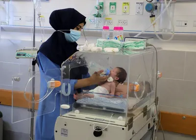 A health worker feeds a premature baby in an incubator