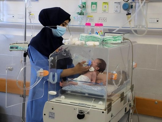 a health worker feeds a premature baby in an incubator