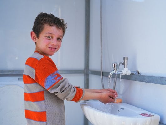 A young boy washes is hands at a sink in an IDP camp in Khan Younis