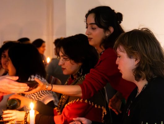 People sit round a long table lit by candles. They share food.