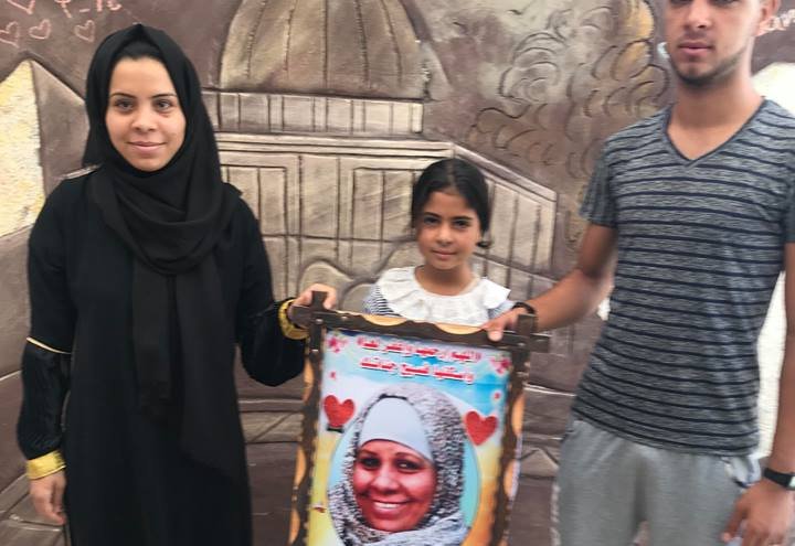 Children of Abeer Abu Jayyab hold a picture of their mother who died in 2017 after being repeatedly denied a permit to travel for breast cancer treatment.
