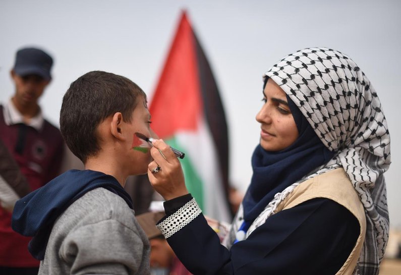 A woman paints a Palestinian flag on a boy's face